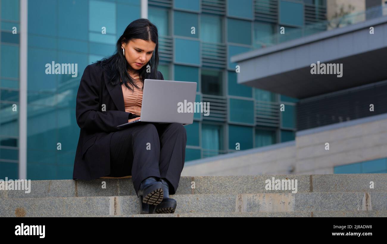 Jeune femme d'affaires hispanique assise à l'extérieur travaillant à distance sur Internet tapant sur ordinateur portable heures supplémentaires en utilisant l'application informatique faisant du travail en ligne Banque D'Images