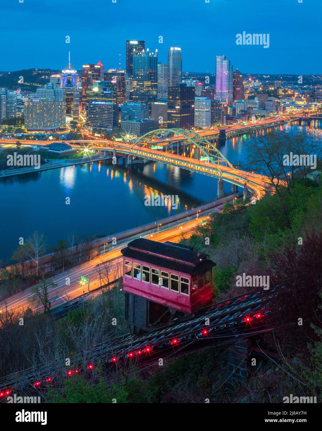 Une voiture rouge et pourpre monte le chemin de fer historique de Duquesne Incline avec la rivière Monongahela et les gratte-ciel de Pittsburgh en arrière-plan la nuit Banque D'Images