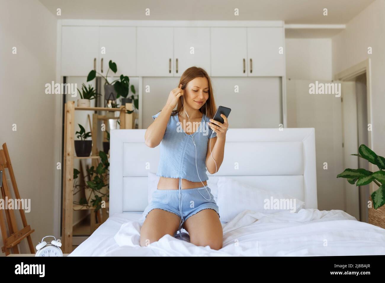 Jeune fille ado en pyjama debout sur son lit et verifier smartphone. Joyeuse jeune fille caucasienne avec des ecouteurs dans sa chambre a coucher Photo Stock Alamy