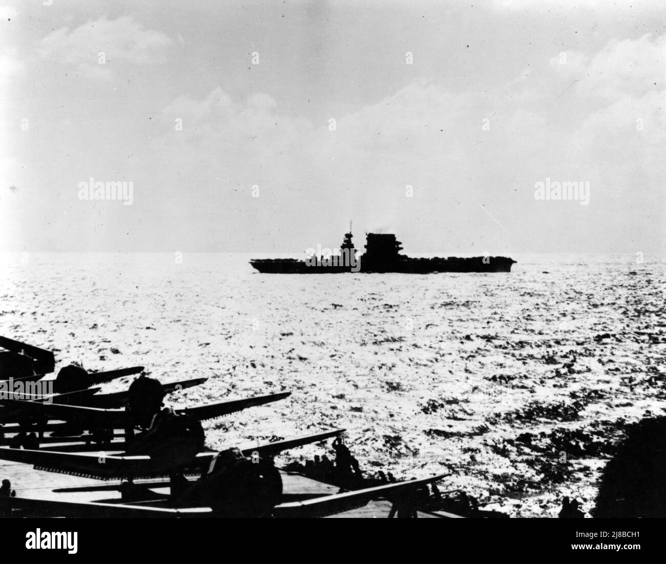 USS Lexington (CV-2) pendant l'action, vu de l'USS Yorktown (CV-5), 8 mai 1942. Un grand nombre d'avions sur le pont et le soleil bas indiquent que la photo a été prise tôt le matin, avant de lancer la grève contre la force aérienne japonaise. Yorktown a plusieurs SBD et F4Fs sur le pont avec des moteurs en marche, apparemment en préparation pour le décollage. Lexington, dont la silhouette a été modifiée par le retrait plus tôt de ses tourelles à canon de 8 pouces, a des avions garés avant et arrière, et peut être en train de forcer son pont en préparation pour lancer l'avion. Banque D'Images