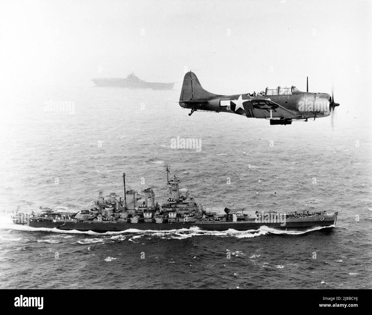 U.S. Navy Douglas SBD-5 Dauntless de l'escadron de bombardement VB-16 vole une patrouille antisous-marine au-dessus du cuirassé USS Washington (BB-56) en route vers l'invasion des îles Gilbert, le 12 novembre 1943. Le navire en arrière-plan est le USS Lexington (CV-16), le porte-avions. Banque D'Images
