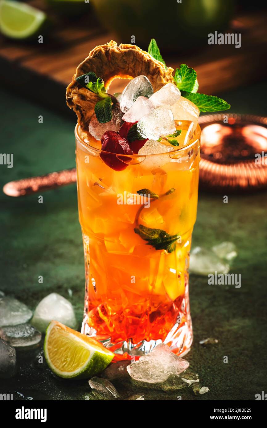 Cocktail alcoolisé avec vodka, jus d'ananas, mangue, sirop rouge et glace.  Boisson longue ou cocktail froid d'été. Arrière-plan tropical foncé avec  feuilles de palmier Photo Stock - Alamy