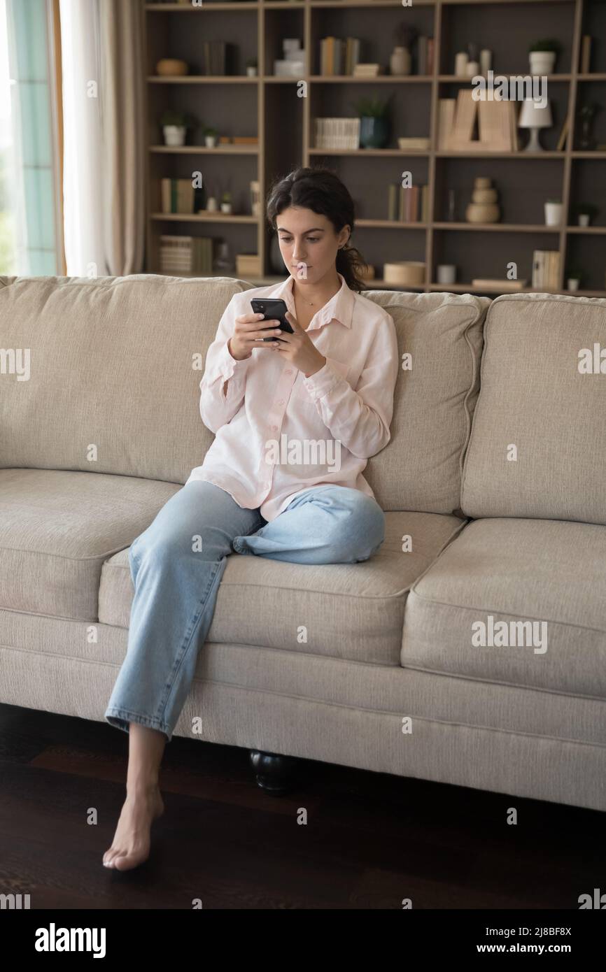 Vue verticale grave adolescente s'asseoir sur le canapé utiliser le téléphone portable Banque D'Images
