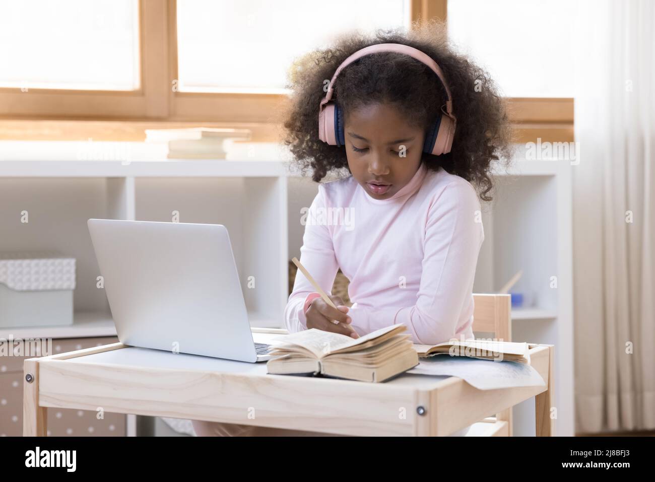 Une fille africaine dans un casque s'assoit à la table pour étudier l'utilisation d'un ordinateur portable Banque D'Images