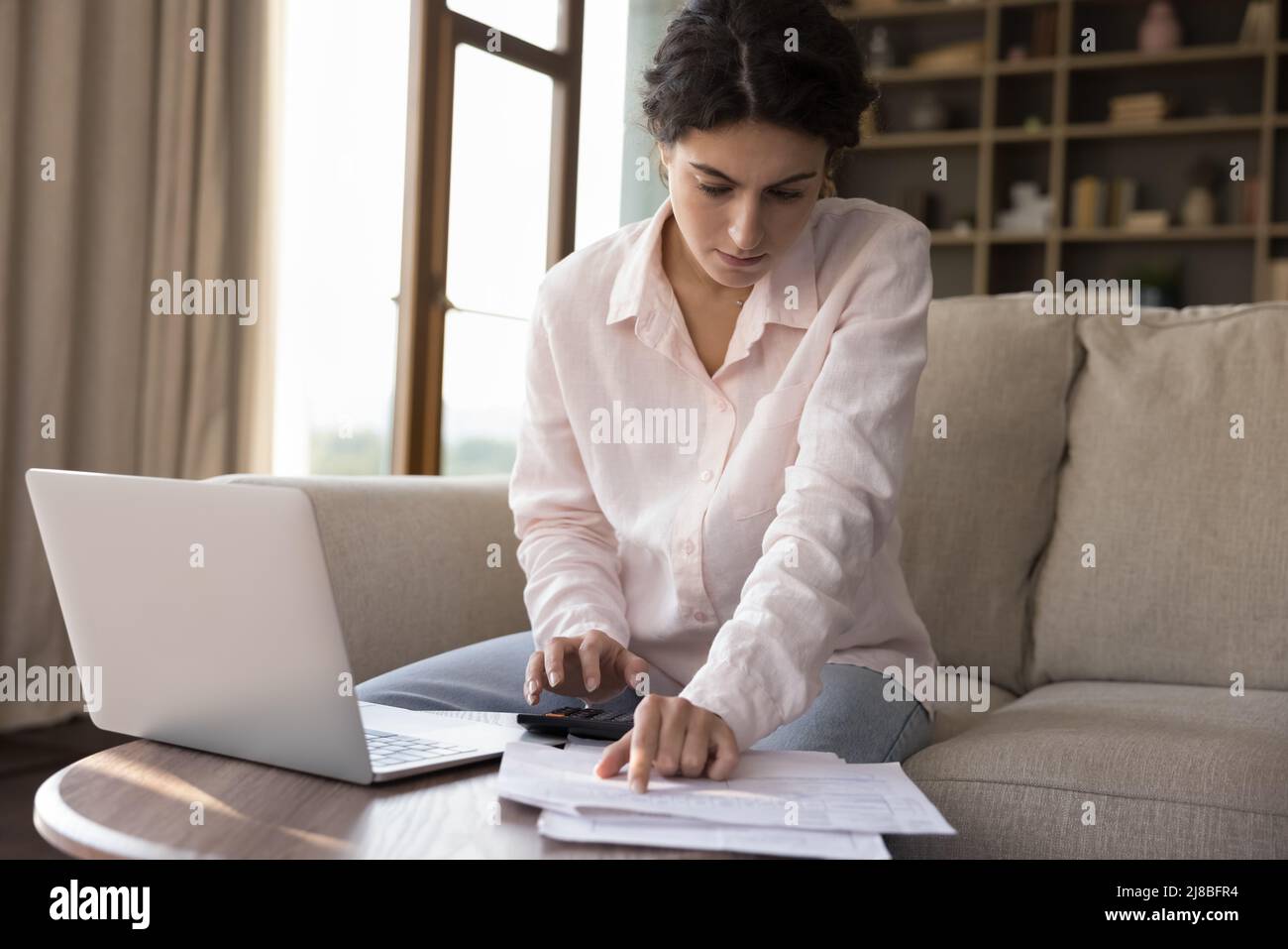 La femme calcule les dépenses sur la calculatrice, paie les factures à l'aide d'un ordinateur portable Banque D'Images