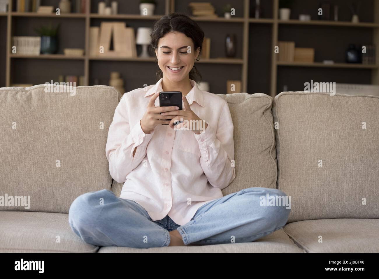 Femme souriante assis sur un canapé avec un smartphone, profitez de la communication en ligne Banque D'Images