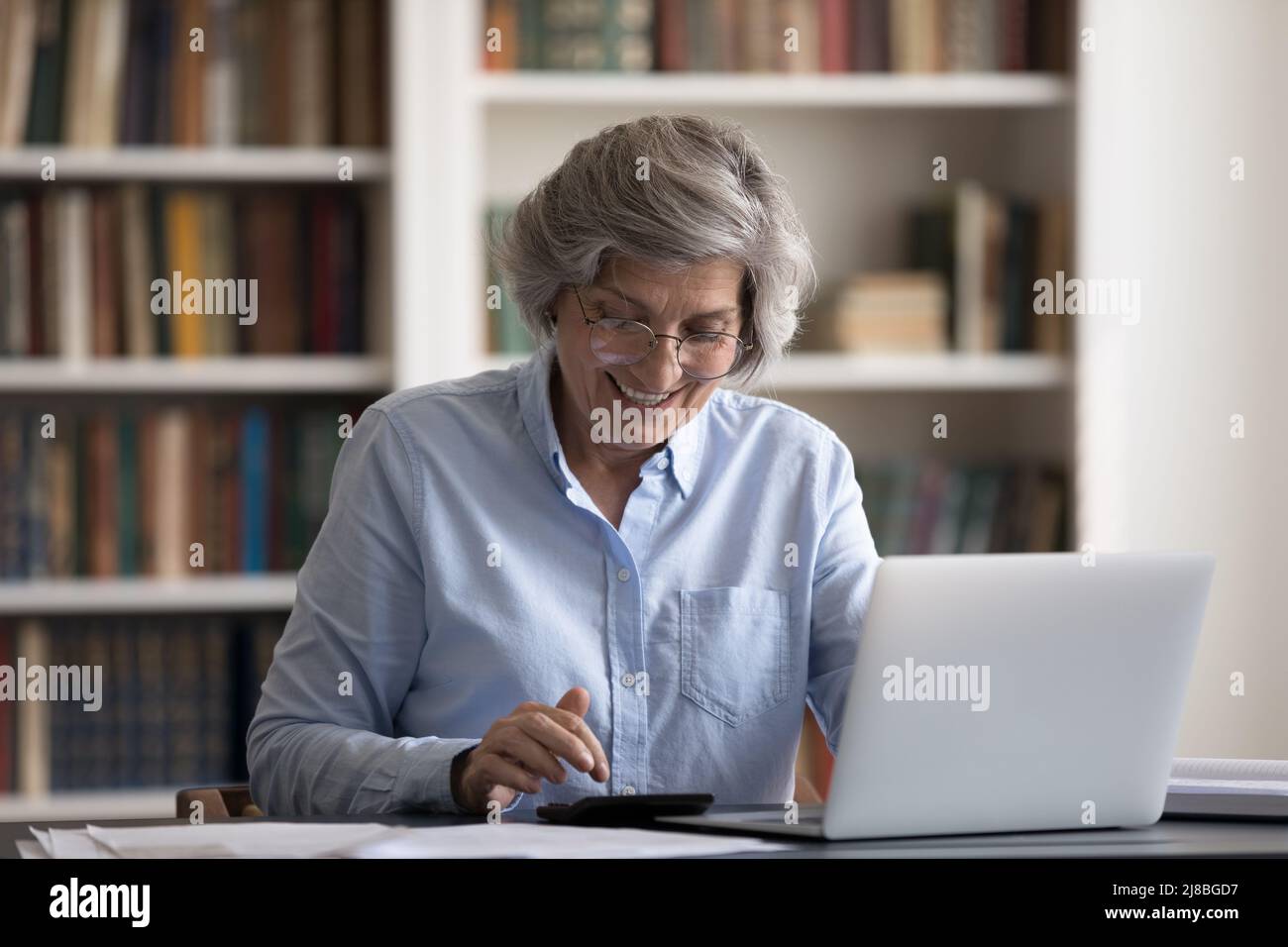 Bonne femme propriétaire senior dans des lunettes en utilisant la calculatrice Banque D'Images