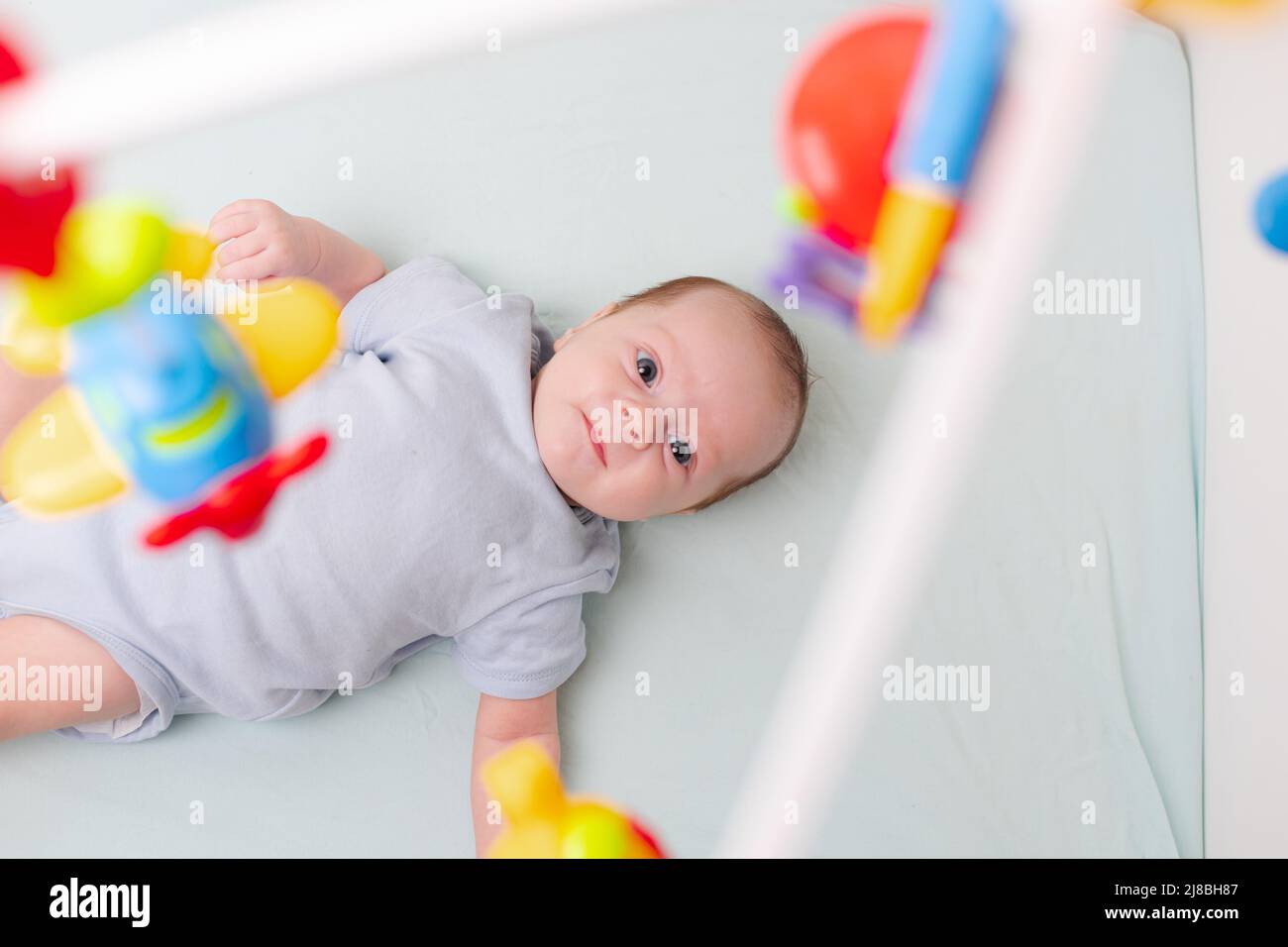 Le bébé regarde le mobile couché dans le berceau . Mobile au lit de bébé. Un article sur les loisirs pour enfants. Les mains de maman sont libres. Un article sur le choix d'un mobile dans le berceau. Le bébé a 0-3 mois. Un bébé Banque D'Images