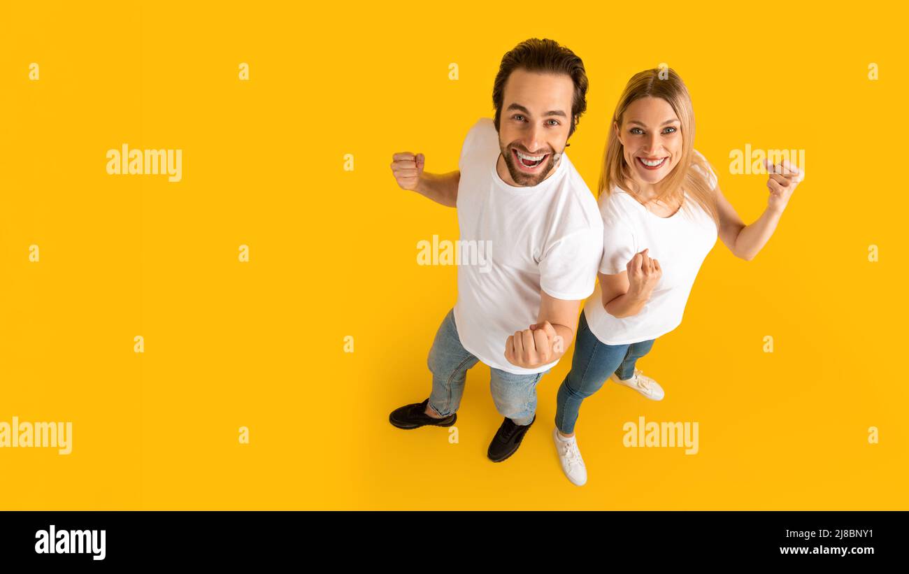 Un jeune homme et une jeune femme européens satisfaits avec des bouches ouvertes dans des t-shirts blancs pointent les doigts sur l'espace de copie Banque D'Images