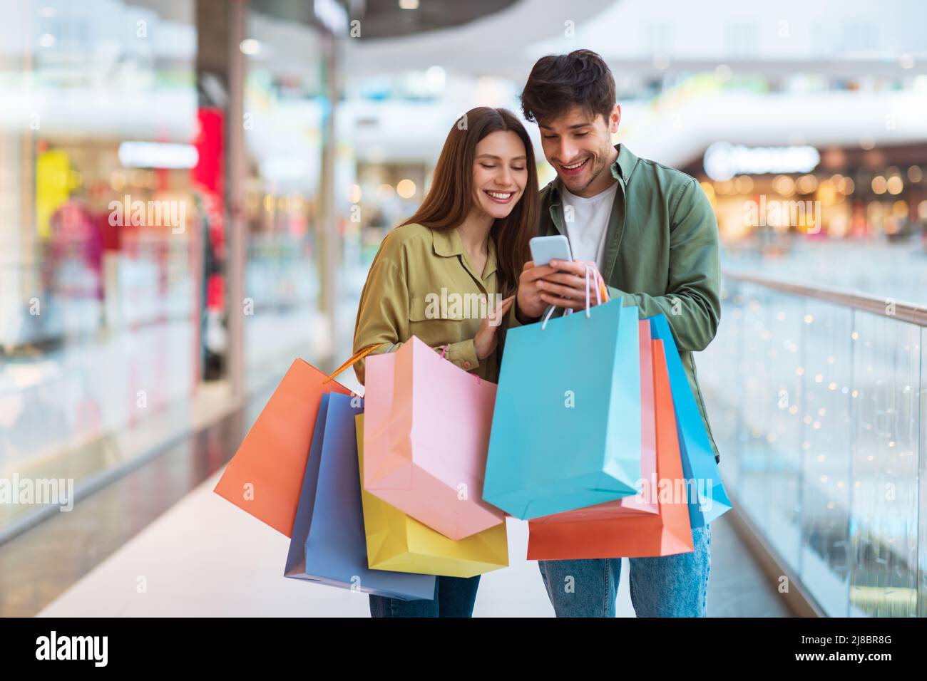 Les conjoints heureux faisant des achats et en utilisant le téléphone portable dans le centre commercial Banque D'Images
