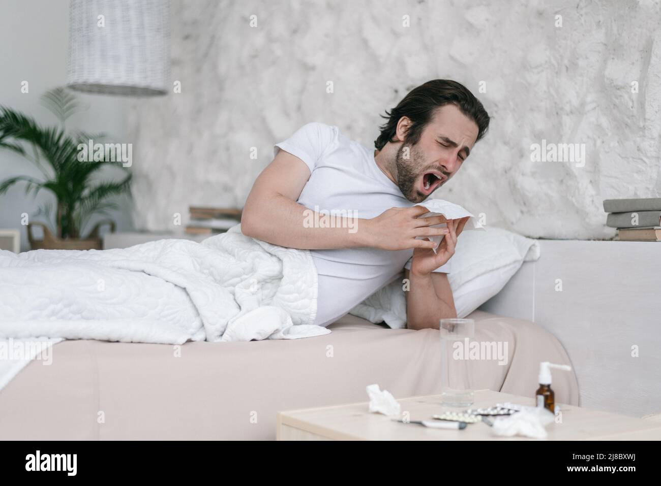 Triste millennal caucasien gars avec chaume se trouve sur le lit, éternue à la serviette dans la chambre à l'intérieur avec des médicaments Banque D'Images