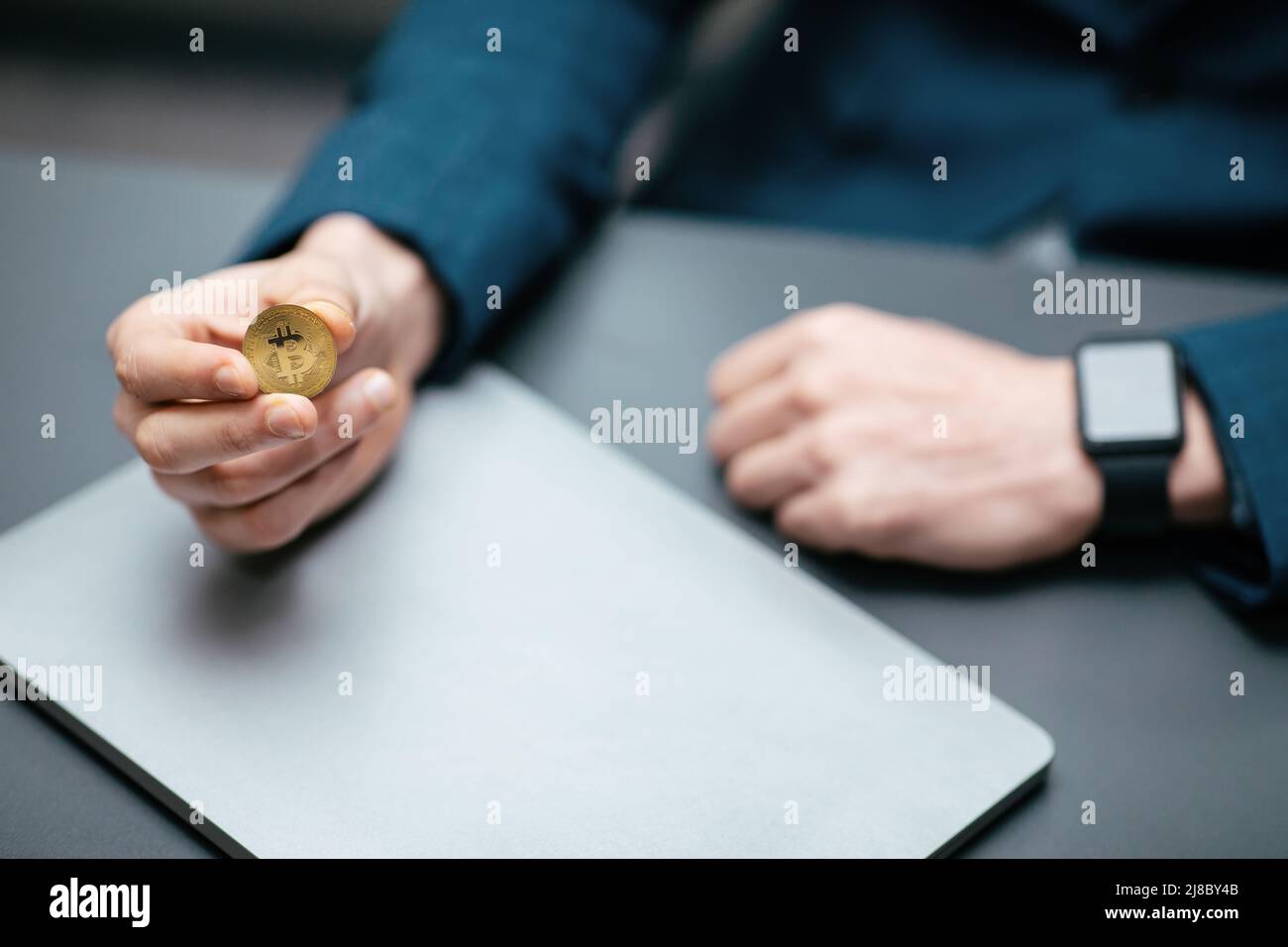 Homme d'affaires en costume avec montre intelligente tient le bitcoin dans sa main dans l'intérieur de bureau, court Banque D'Images