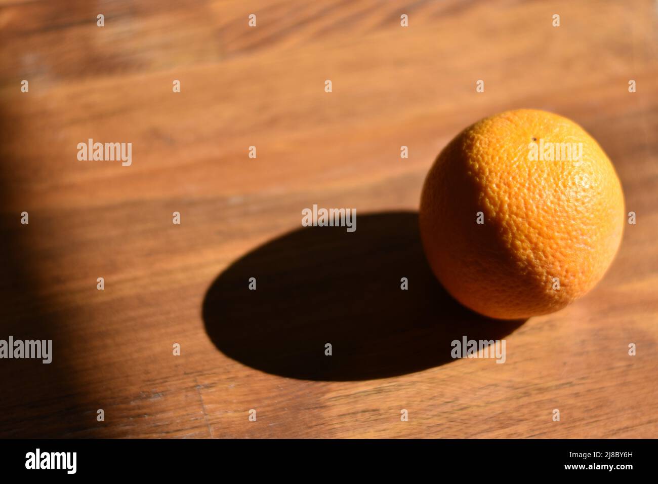 Orange mûr avec ombre sur une table en bois Banque D'Images