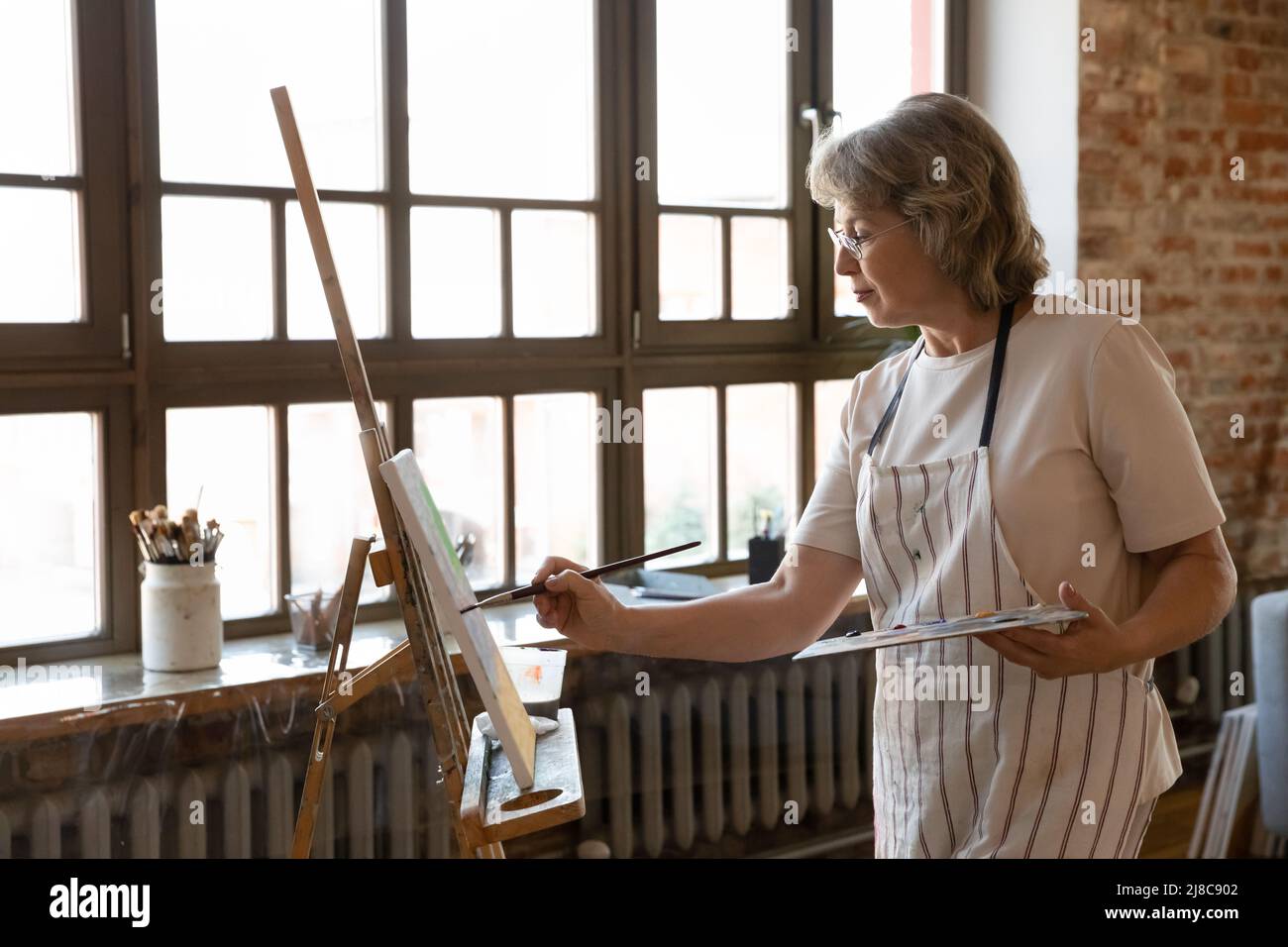 Femme plus âgée peignant sur un chevalet en atelier Banque D'Images