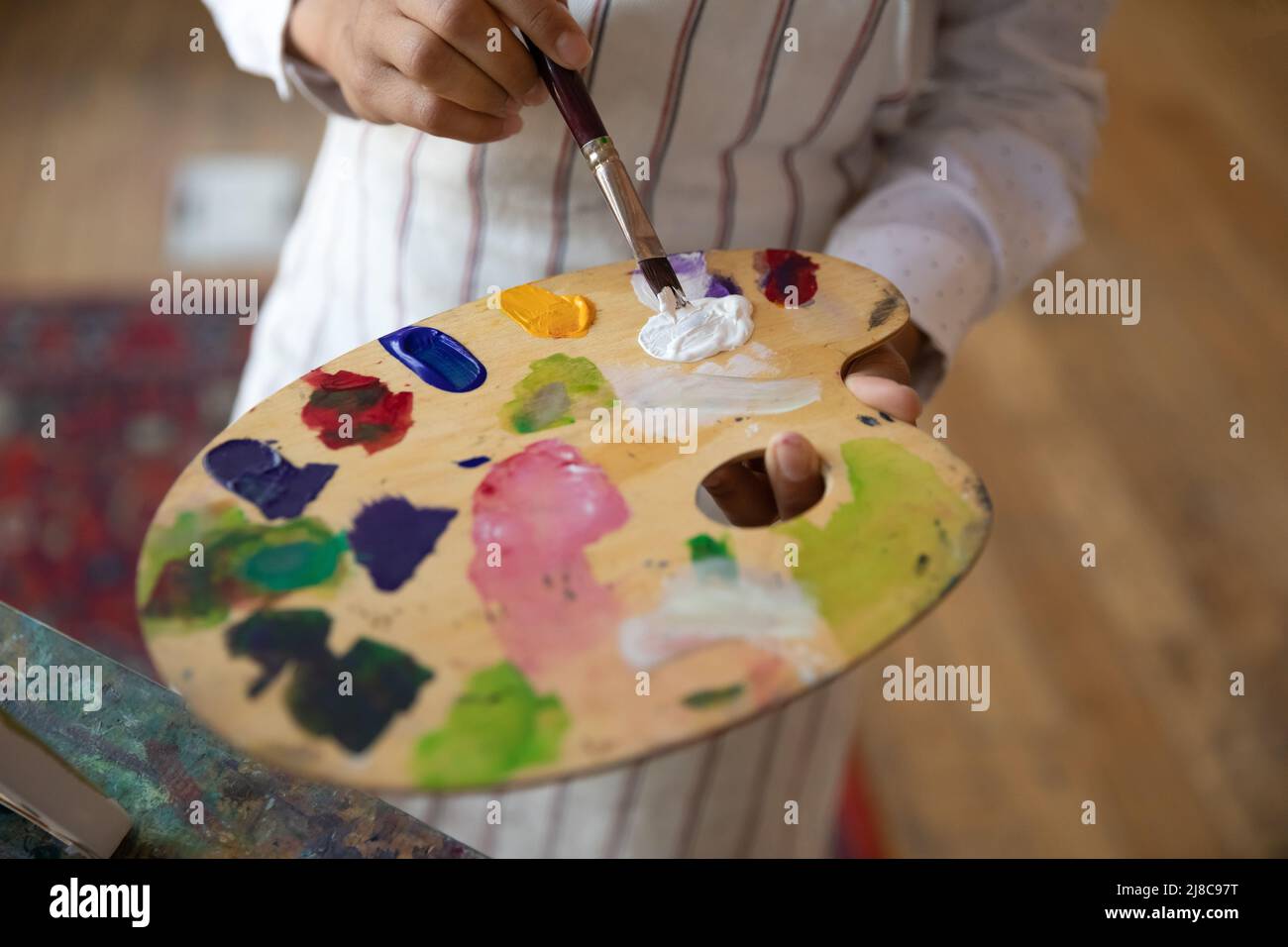 Femme peintre tenant pinceau mélange des couleurs sur palette de bois, gros plan Banque D'Images
