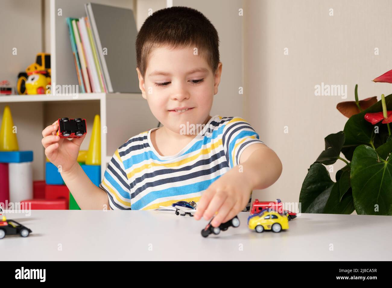 Un enfant d'âge préscolaire joue avec des voitures jouets assises à une table à la maison. Banque D'Images