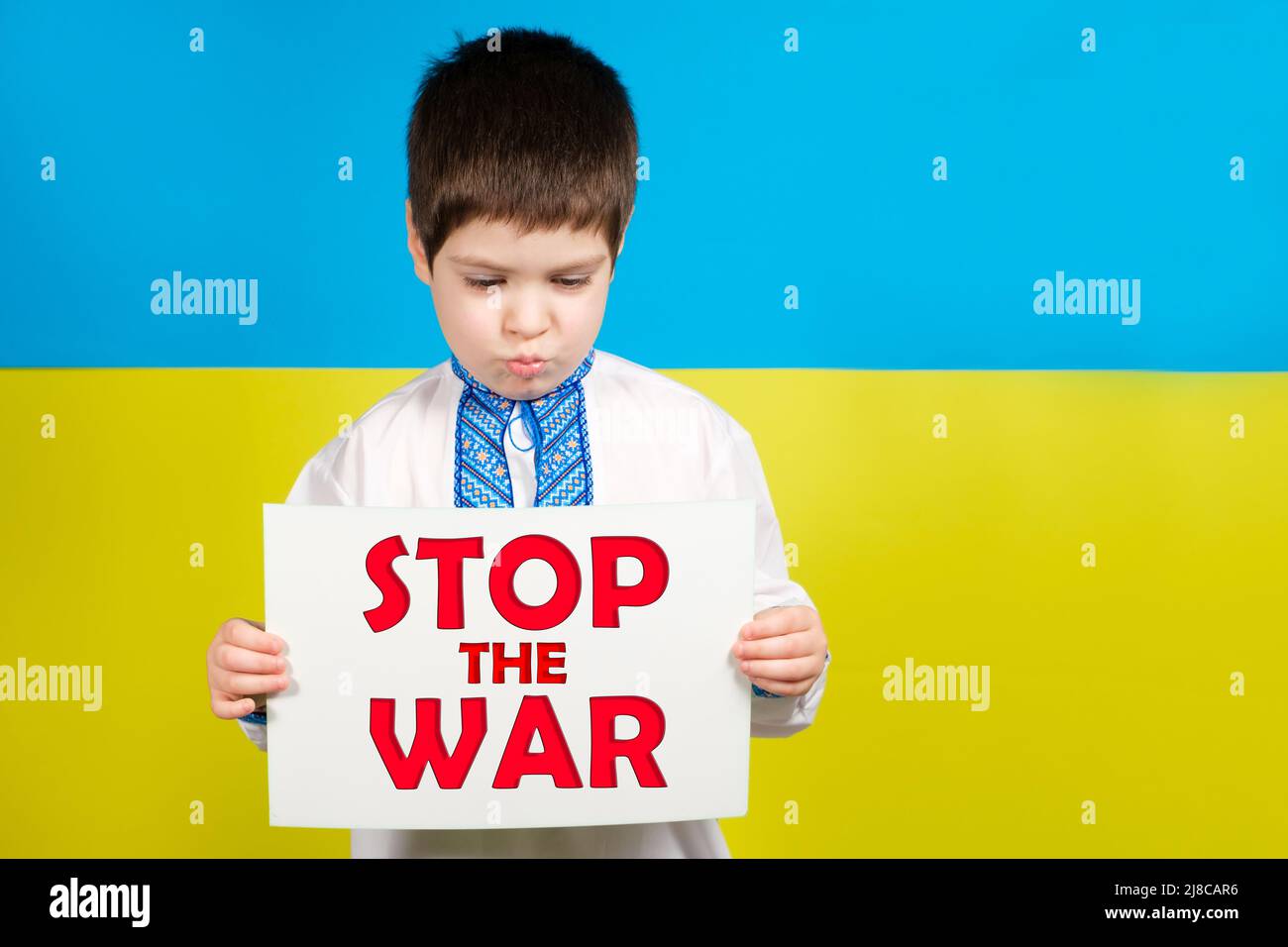 Un garçon ukrainien de 4 ans possède une feuille avec le texte Stop the War sur fond de drapeau bleu-jaune, lieu pour le texte. Banque D'Images