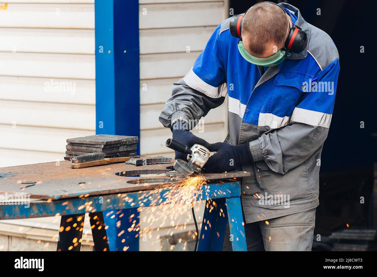 Un vrai travailleur dans les vêtements de travail grince la surface métallique et des étincelles volent. Portrait réel de la personne au travail Banque D'Images