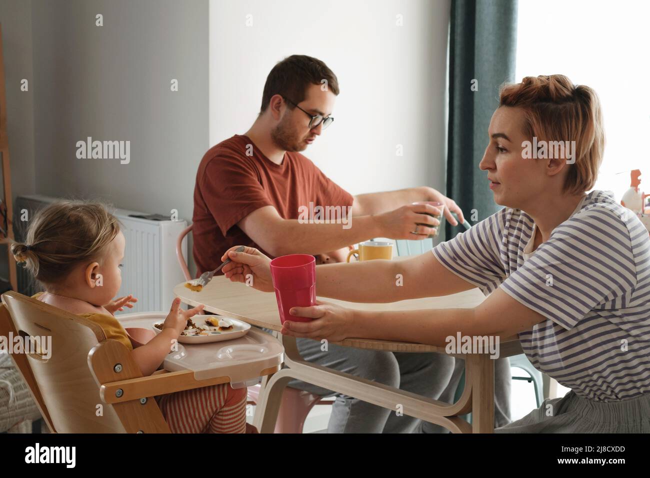 Parents avec enfants en repas, petit déjeuner à table. Mère servant de la nourriture à la famille à la maison. Manger avec les enfants. Fille en chaise haute manger Banque D'Images