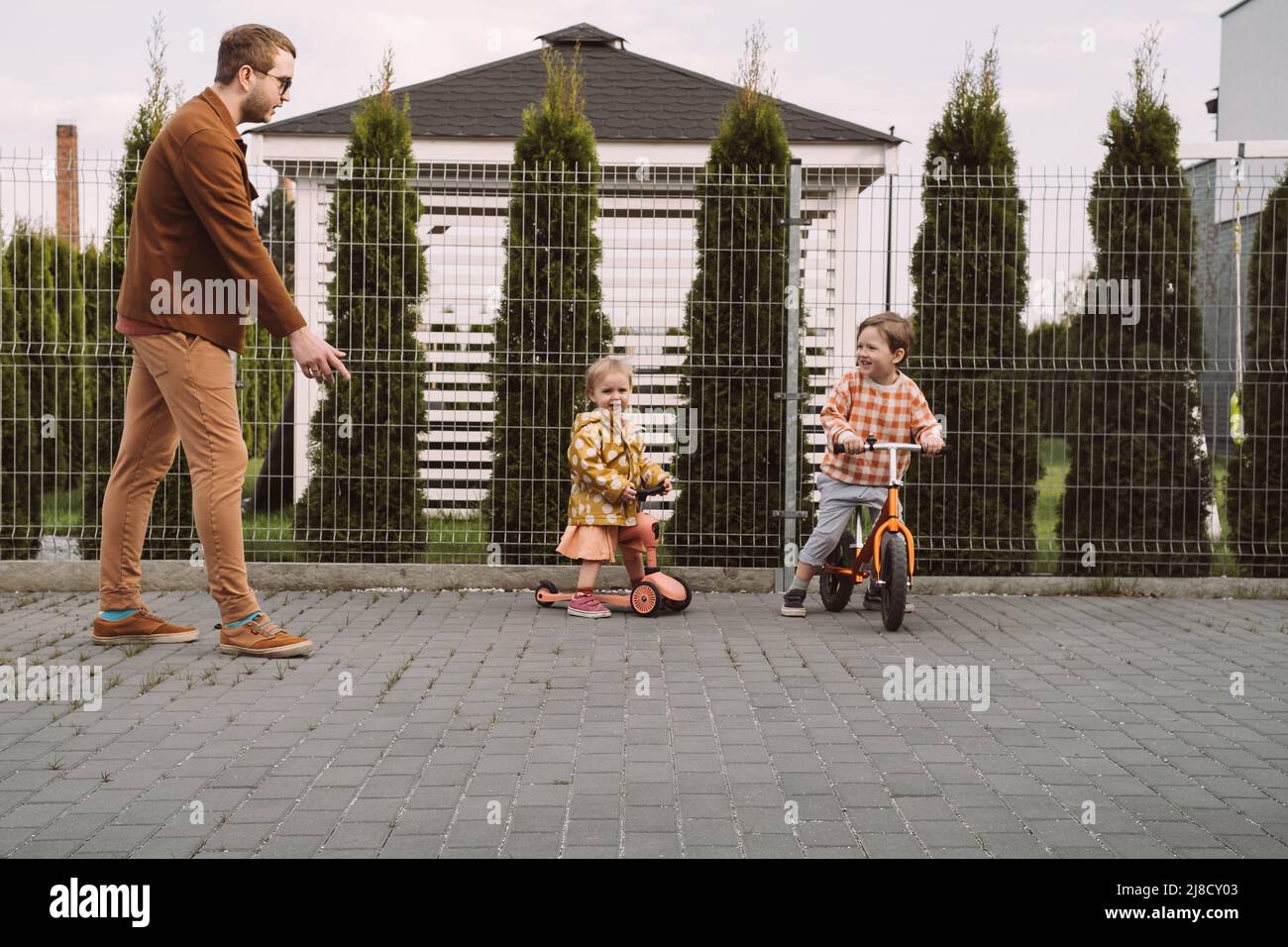 Enfants jouant à la course de vélo et de scooter dans la cour de la maison. Sœur et frère à cheval rapide autour de la maison privée. Concours de frères et sœurs de famille. Enfants Banque D'Images