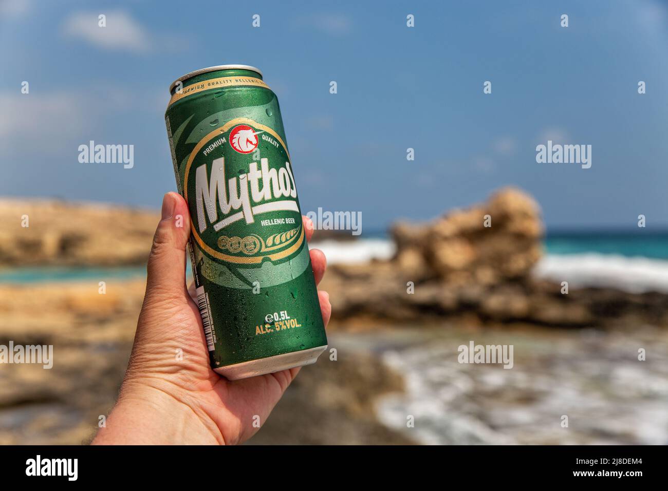 Ayia Napa, Chypre - 29 mai 2021 : la main de l'homme blanc tient une canette de bière chypriote Mythos à proximité de la plage de la station balnéaire d'Ayia Napa en arrière-plan. Banque D'Images