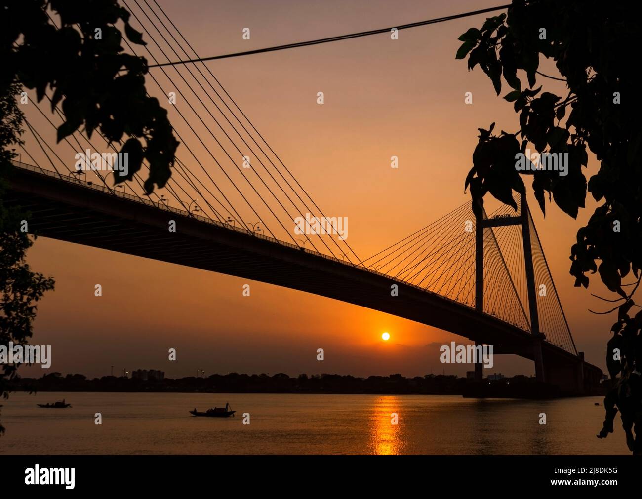 Silhouette de Vidyasagar Setu, Kolkata en soirée. Cadre ensoleillé avec bateau passant sur le Gange. Mise au point sélective. Banque D'Images