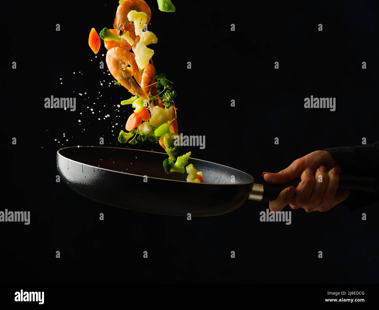 Crevettes tigrées avec des tranches de citron, des légumes et des herbes dans une poêle à frire. Nourriture dans un vol gelé sur fond noir. Le processus de cuisson des fruits de mer wi Banque D'Images