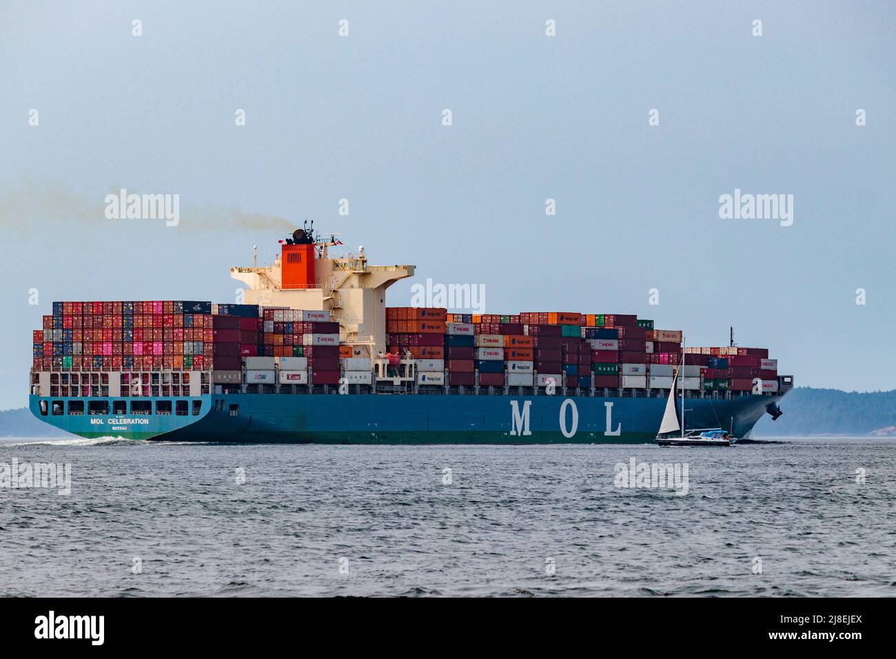 Un voilier est nain à côté de l'immense navire à conteneurs chargé « OL Celebration », en cours à Boundary Pass, dans le sud de la Colombie-Britannique Banque D'Images
