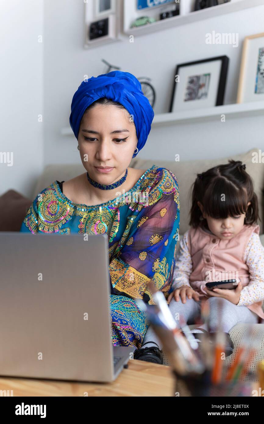 Femme seule travaillant à la maison avec un ordinateur portable. Mère et fille utilisant la technologie. Famille monoparentale. Banque D'Images