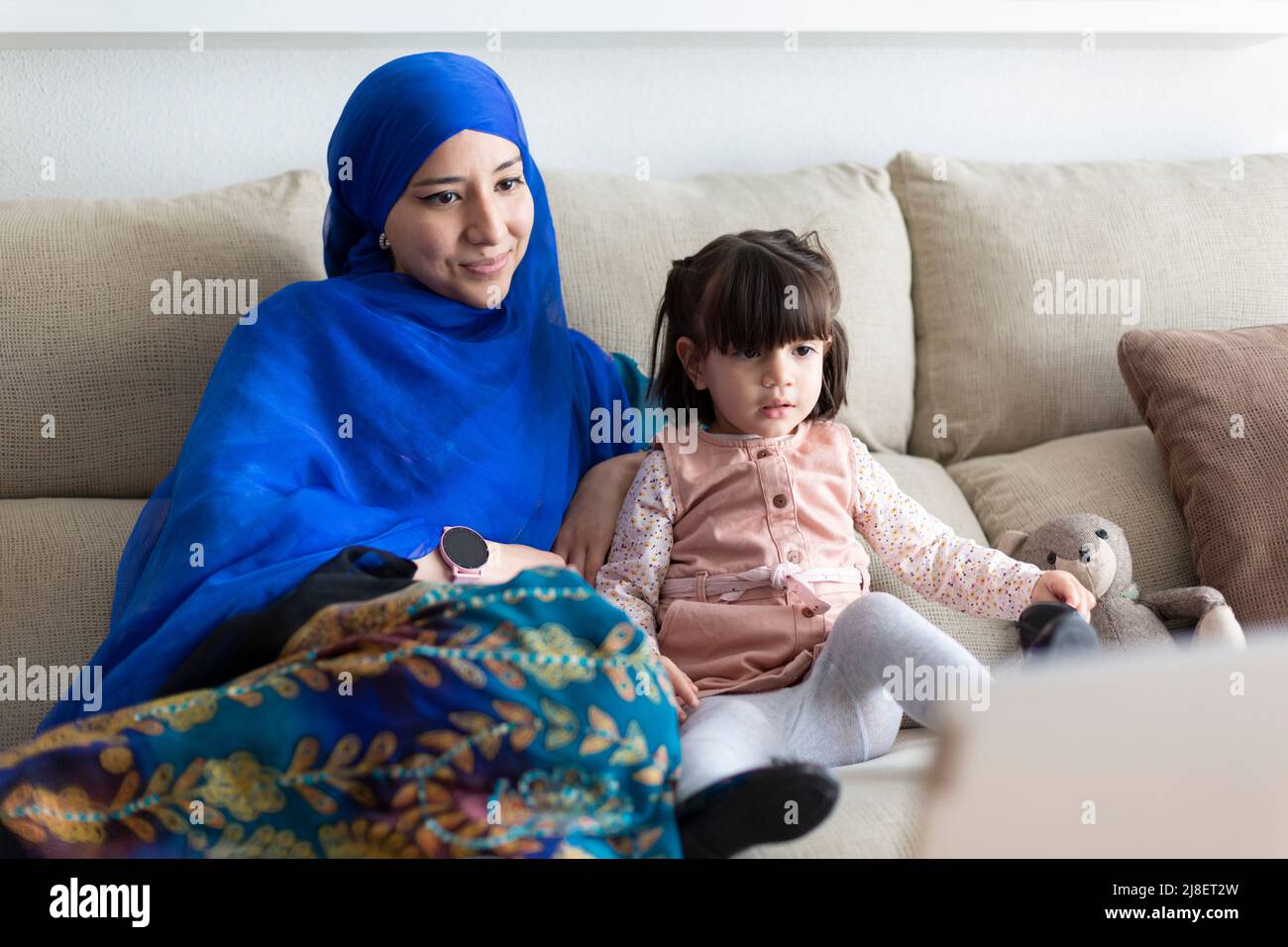 Jeune femme musulmane avec sa jeune fille à la maison. Une famille de parents qui regardent des dessins animés sur un ordinateur portable. Banque D'Images