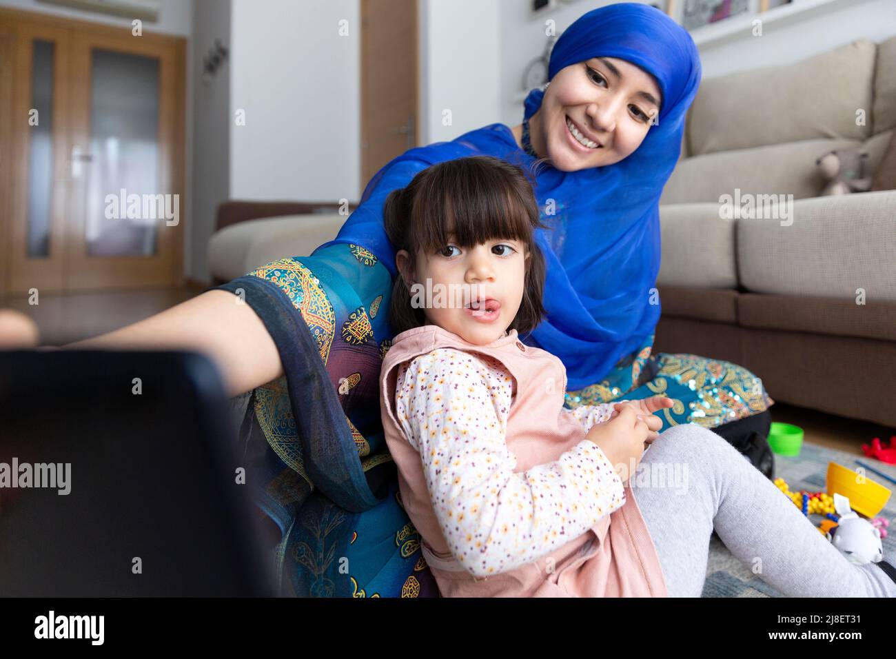 Une jeune femme musulmane prend une photo avec sa fille pendant qu'elle joue dans le salon. Loisirs à la maison. Banque D'Images