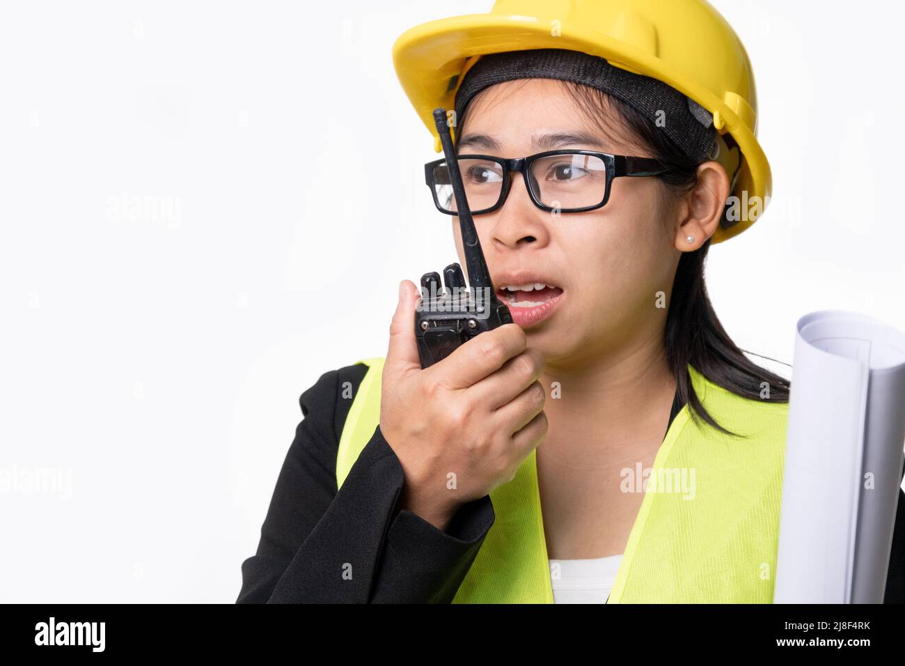 Femme ingénieur civil dans un casque tenant des plans de construction et utilisant walkie-talkie et parler à d'autres membres du personnel sur un fond blanc en studio. Banque D'Images