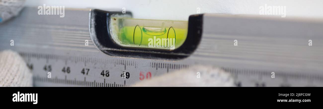 Les mains du travailleur vérifient la planéité du mur à l'aide d'un outil spécial pour mesurer le niveau. La scène de face au mur de la cuisine avec des carreaux de céramique blanche Banque D'Images