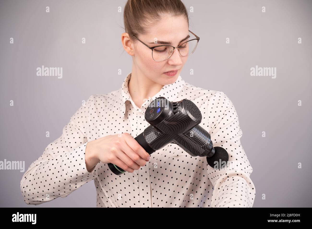 Femme d'affaires caucasienne massant son biceps avec un masseur à percussion. Banque D'Images