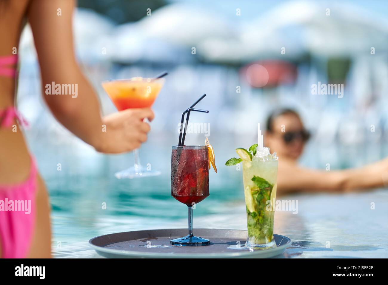 Deux cocktails frais sur plateau rond près de la piscine. Vue rognée de la main des femmes tenant le verre avec une boisson tout en se refroidissant à la piscine, avec complexe flou sur l'arrière-plan. Concept de rafraîchissement. Banque D'Images
