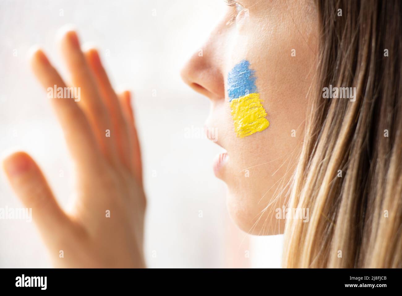 Une femme ukrainienne avec le drapeau national de l'Ukraine jaune-bleu sur son visage regarde par la fenêtre, patriote, la paix en Ukraine, la loi martiale, je vois la wa Banque D'Images