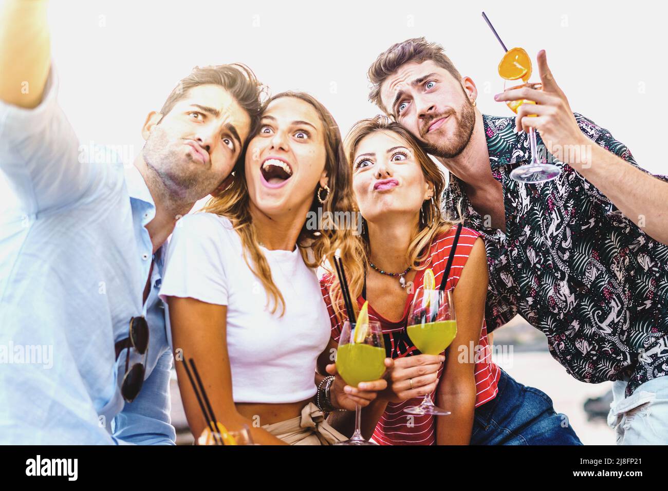 Heureux ivres amis prenant un selfie faisant des visages tenant des cocktails alcoolisés assis sur un banc à l'extérieur en été - amour de l'amitié en happy hour Banque D'Images