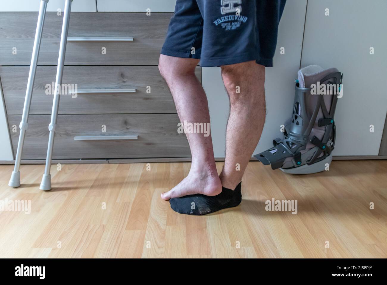 L'homme européen après l'opération de rupture de tendon d'Achille est de retour à la maison avec la chaussure de physiothérapie spéciale de botte de lune et des béquilles pour la récupération à la maison contre Banque D'Images