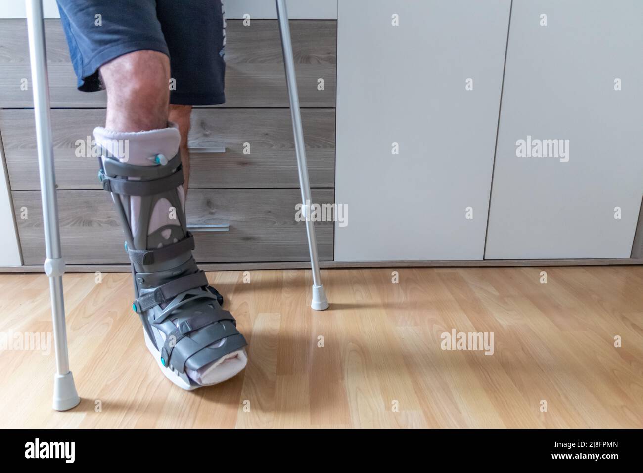 L'homme européen après l'opération de rupture de tendon d'Achille est de retour à la maison avec la chaussure de physiothérapie spéciale de botte de lune et des béquilles pour la récupération à la maison contre Banque D'Images