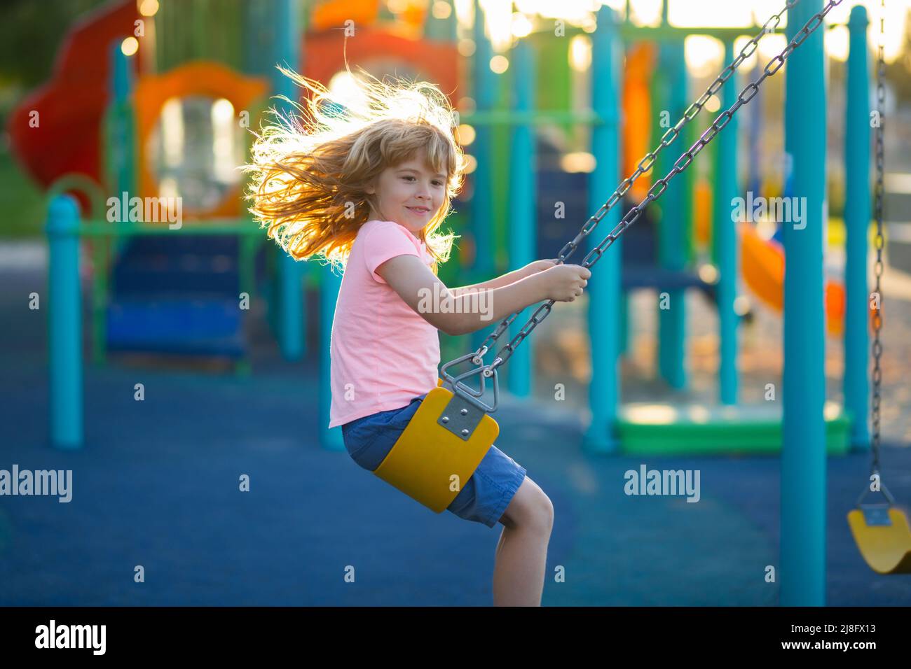 Enfant balançant sur l'aire de jeux. Enfants jouant sur l'aire de jeux de la maternelle. Joyeux enfant sur l'aire de jeux. Aire de jeux pour enfants avec balançoire, toboggan Banque D'Images
