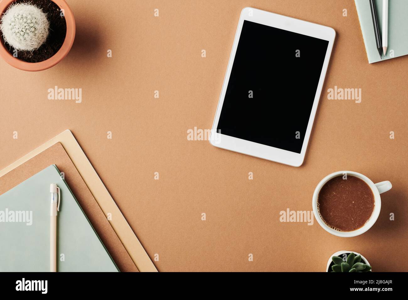 Partie de l'espace de travail de designer moderne avec tablette, tasse de café, carnet avec stylo sur le dessus, plantes dans pots de fleurs et crayons sur le livre d'auteur Banque D'Images