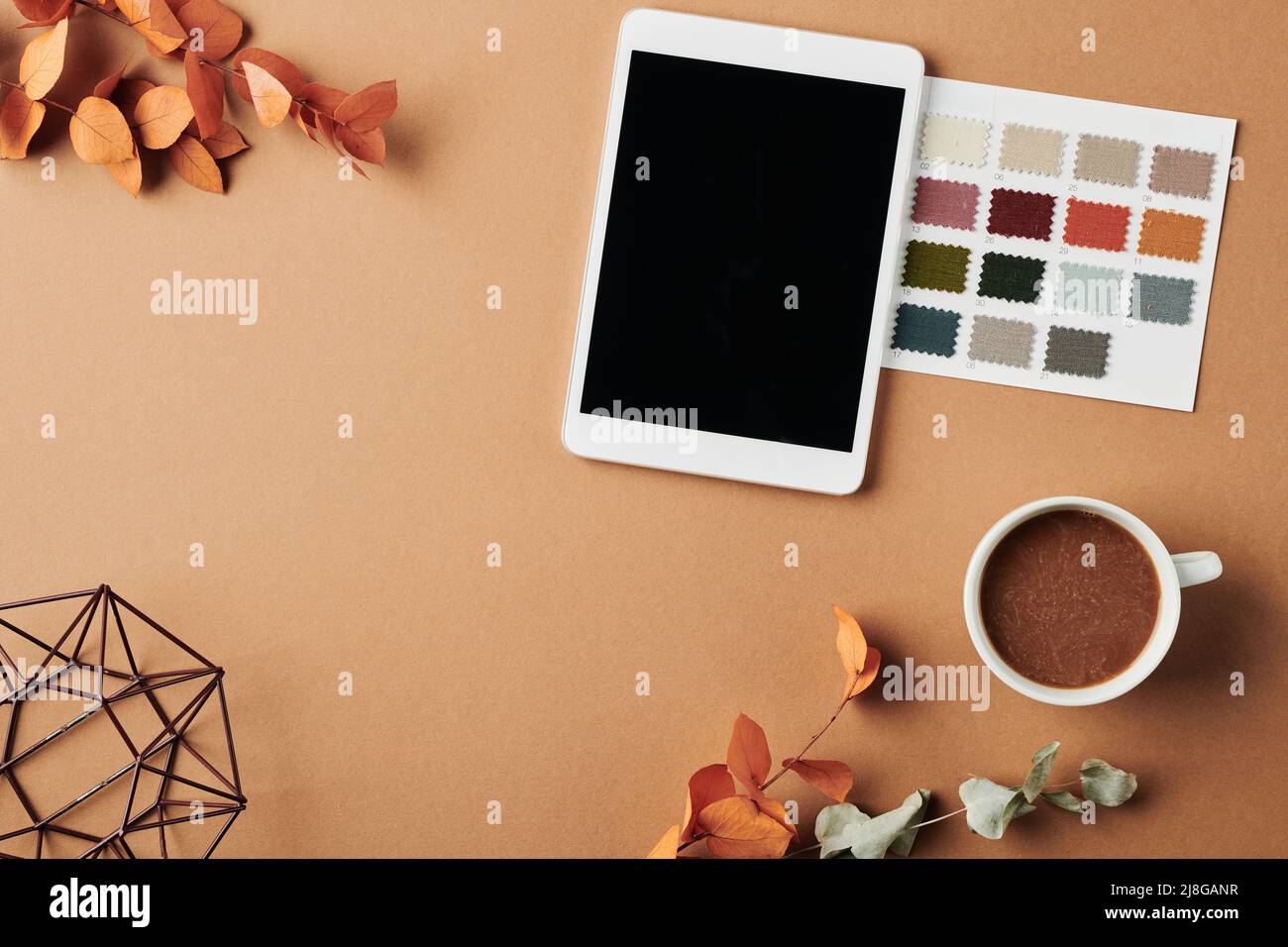 Vue de dessus de l'espace de travail du designer avec tablette, nuances de couleurs, tasse de café, vase fait à la main et feuilles d'orange sèches sur une table beige Banque D'Images