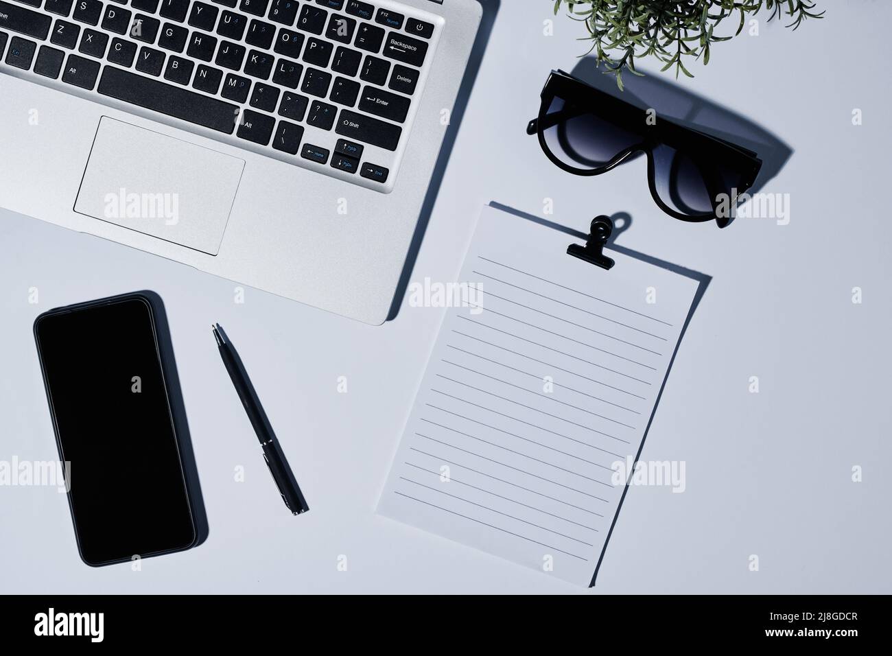 Composition d'un clavier d'ordinateur portable, papier vierge avec clip, lunettes de soleil, stylo, et smartphone sur le lieu de travail de la personne d'affaires moderne Banque D'Images