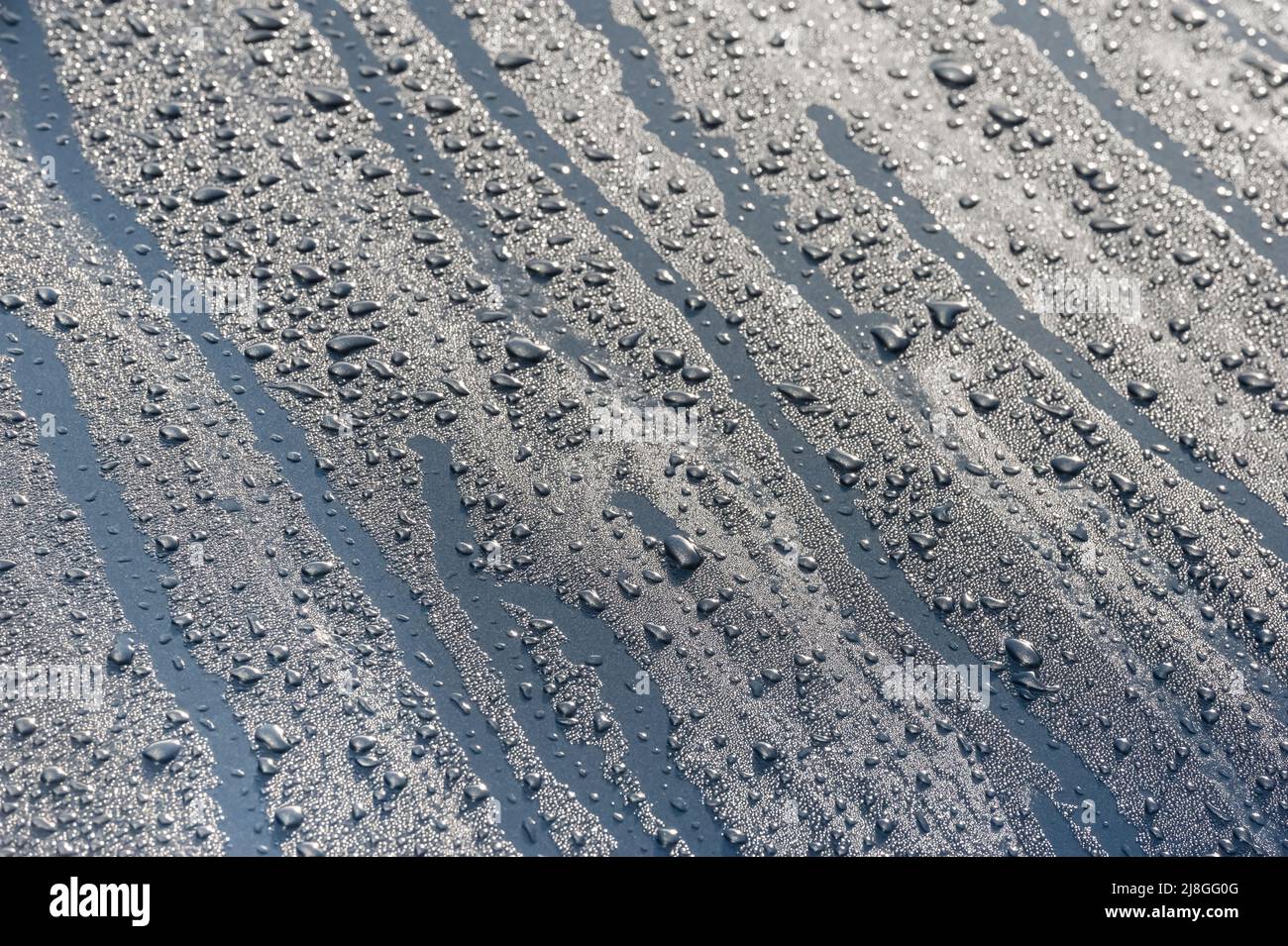 gouttes de pluie sur un capot métallique sous un ciel bleu Banque D'Images