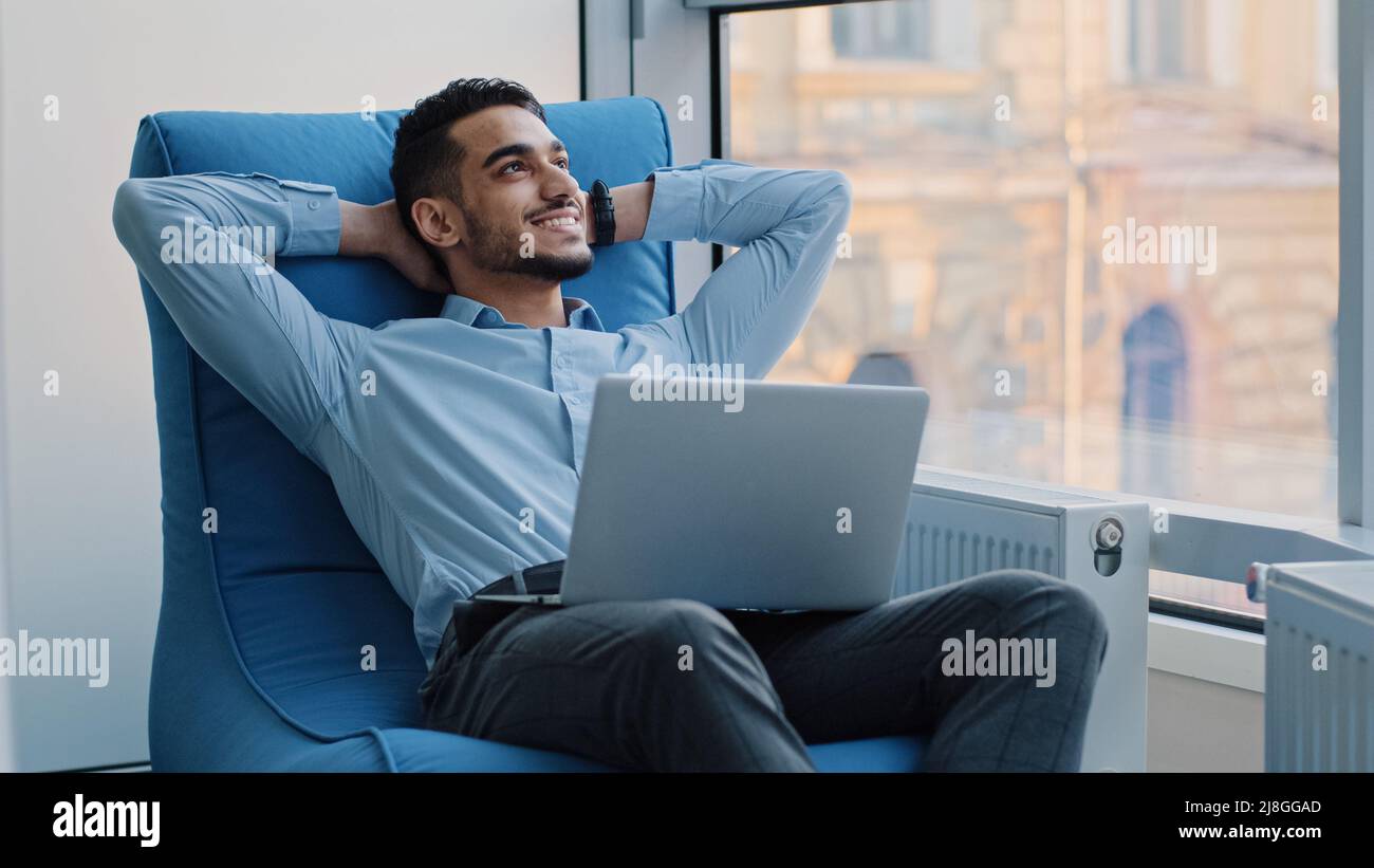 Jeune arabe professionnel travaillant sur ordinateur portable, rêver, créer une nouvelle idée. Un employé indien millénaire souriant dans une profession créative s'assoit confortablement Banque D'Images