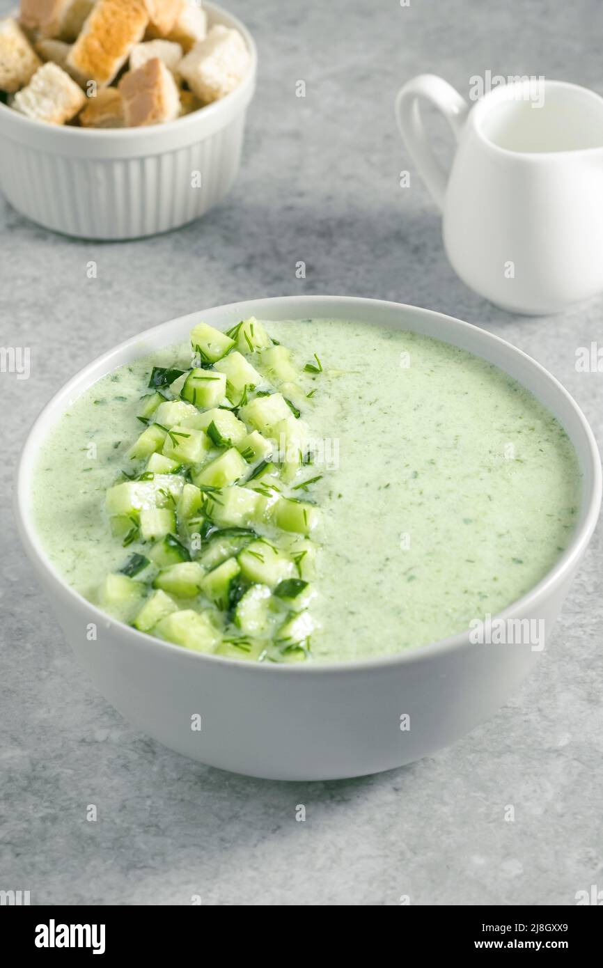 Soupe d'été fraîche et verte avec concombre, croûtons et crème sur fond gris. Concept de cuisine végétalienne Banque D'Images