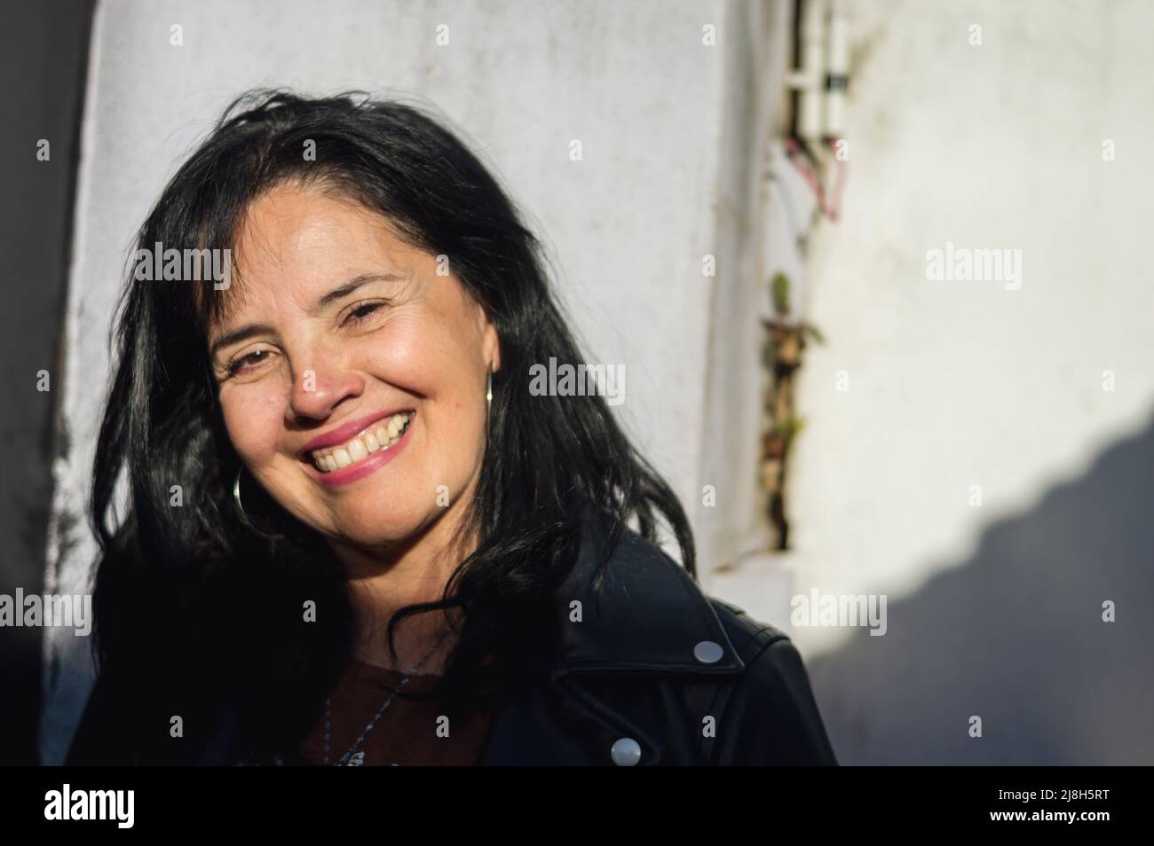 portrait femme adulte caucasienne, souriant et regardant l'appareil photo, debout à l'extérieur dans le patio ensoleillé de la maison. Banque D'Images