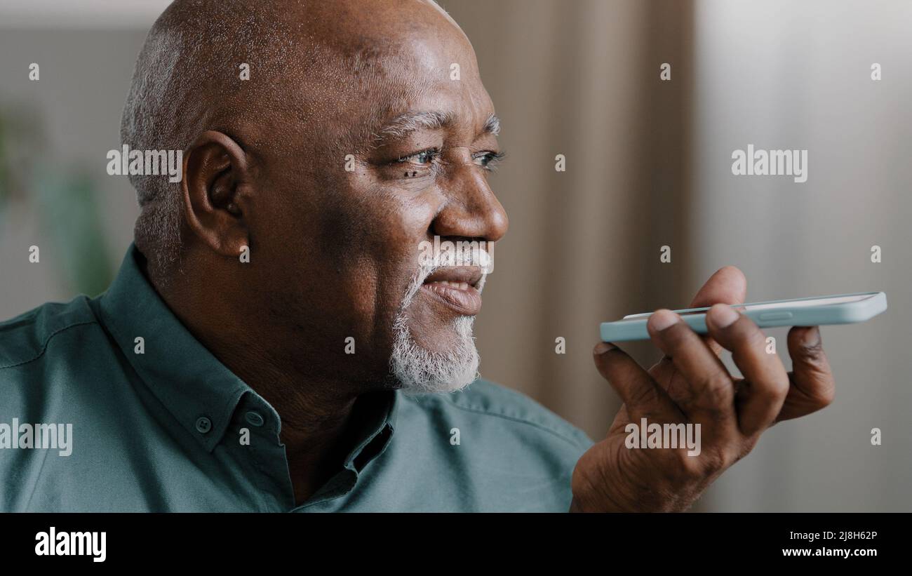 Homme biracial 60s à cheveux gris mûr avec barbe afro-américain ancien homme à la maison tenir le smartphone parler au téléphone microphone haut-parleur voix audio Banque D'Images