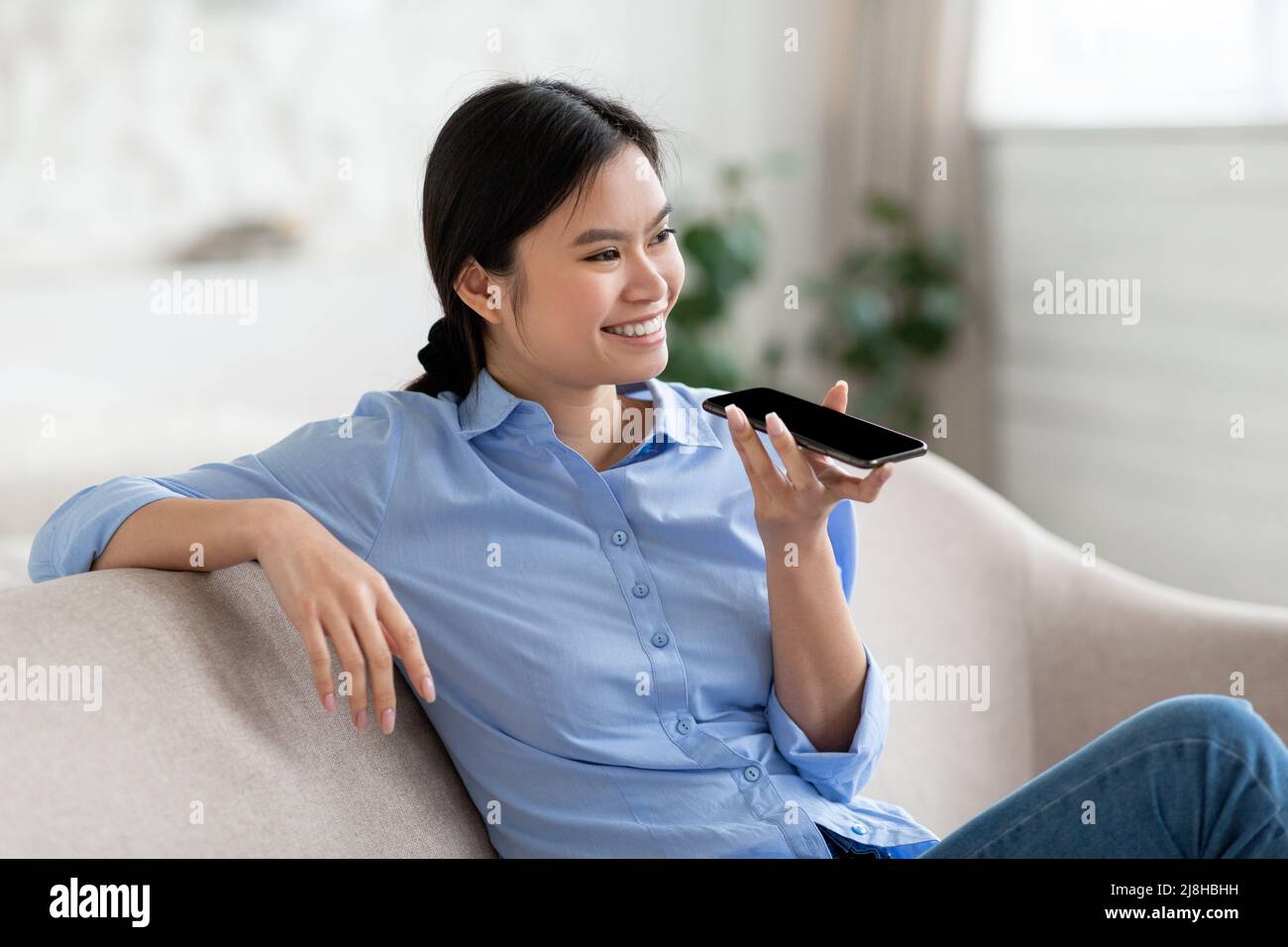 Gros plan d'une femme asiatique joyeuse tenant un smartphone et enregistrant un message vocal Banque D'Images