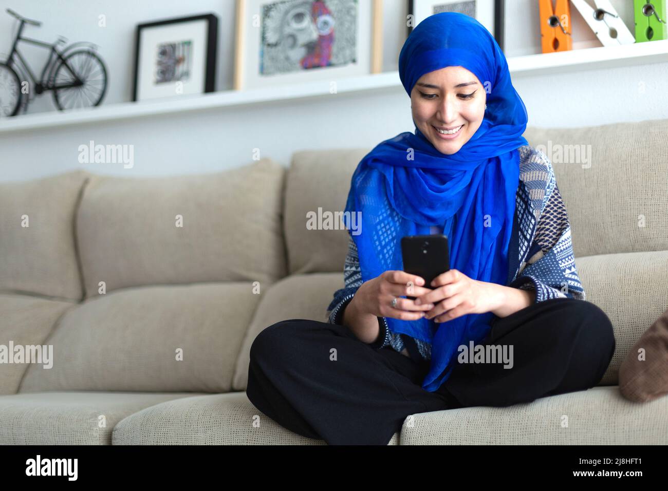 Jeune femme musulmane souriante utilisant un smartphone à la maison. Espace pour le texte. Banque D'Images